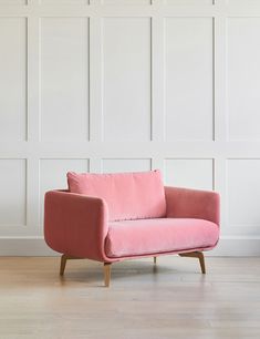 a pink chair sitting on top of a hard wood floor next to a white wall