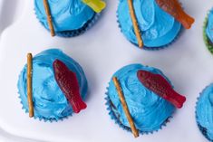 cupcakes decorated with blue frosting and red fish on sticks are arranged in rows