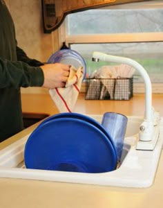 a person washing dishes in a kitchen sink with a blue strainer on the side