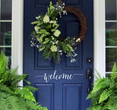 a blue front door with two plants and a wreath on it that says hello in white lettering