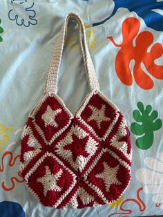 a crocheted red and white purse sitting on top of a bed next to a pillow