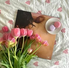 pink tulips are in a vase next to a magazine on a white sheet