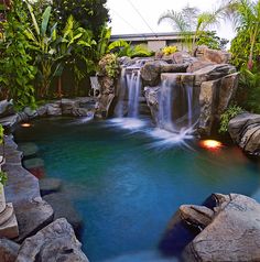 an outdoor pool with waterfall and rocks in the middle, surrounded by greenery on both sides