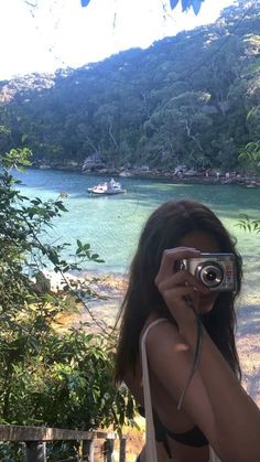 a woman taking a photo in front of a body of water with a small boat