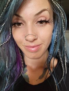 a close up of a person with blue hair and piercings on her nose, smiling at the camera