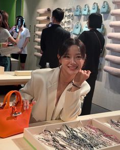 a woman sitting at a table with an orange purse in front of her and several other people standing around