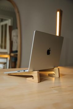 an apple laptop sitting on top of a wooden stand with a mirror in the background