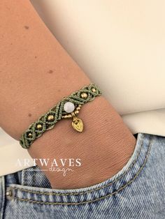 a woman wearing a green bracelet with gold charms on it's wrist and holding onto her arm