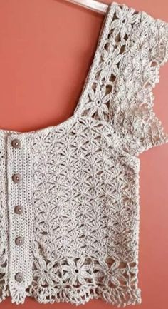 a white crocheted top hanging on a pink wall