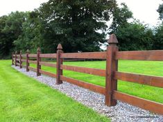 a wooden fence in the middle of a grassy area with gravel and rocks around it