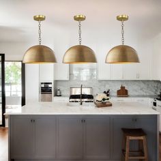 three pendant lights hanging from the ceiling over an island in a kitchen with white cabinets and marble countertops