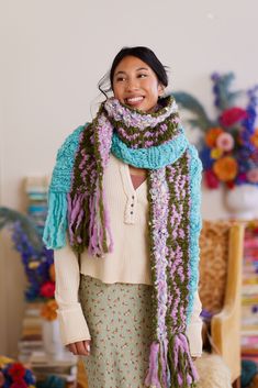 a woman standing in front of a chair wearing a knitted scarf with fringes