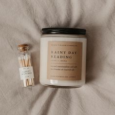 a jar of reading material next to an empty candle on a white sheet with a label that says rainy day reading