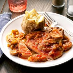 a white plate topped with meat covered in sauce next to potato wedges and a fork