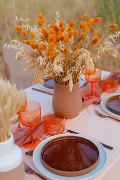 the table is set with plates, cups and vases filled with flowers on it