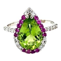 Peridot Diamond and Pink Sapphire White Gold Cocktail Ring  This beautiful ring has a Pear Cut Peridot in the center that weighs 2.77 carats. The ring is surrounded by a cute halo of alternating diamonds and pink sapphires. There are 21 Round Cut Natural Diamonds that weigh 0.31 carats and 14 Pink Sapphires that weigh 0.26 carats. The total carat weight of the ring is 3.34 carats. The diamonds have a clarity of SI and color of F. The setting is crafted in 14K White Gold and weighs 2.9 grams. Thi Pear-shaped Green Diamond Ring With Center Stone, Green Cluster Diamond Ring With Center Stone, Green Brilliant Cut Pear-shaped Diamond Ring, Green Cluster Rings With Brilliant Cut, Green Pear-shaped Diamond Ring With Brilliant Cut, Green Pear-shaped Brilliant Cut Diamond Ring, Green Diamond Ring Pear-shaped, Green Cluster Ring With Halo Setting, Green Halo Setting Cluster Ring Fine Jewelry