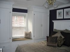 a bed room with a neatly made bed and white cupboards next to a window