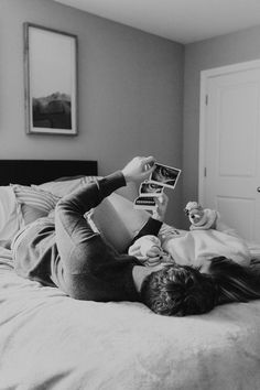 a woman laying on top of a bed holding an open book and looking at it