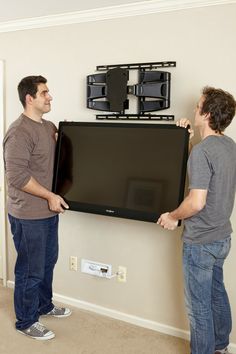 two men standing next to each other in front of a flat screen tv mounted on the wall