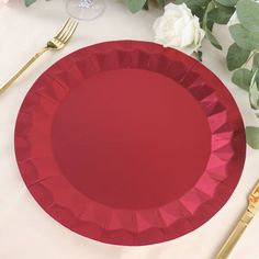 a red plate sitting on top of a table next to silverware and flowers in vases