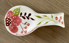 a ceramic toothbrush holder with flowers and leaves painted on the side, sitting on a wooden surface