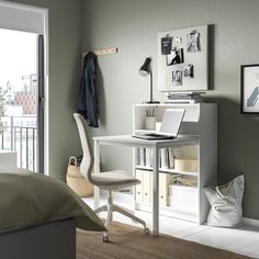 a white desk with a laptop on it in a room next to a bed and window