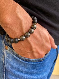 Fortune and Strength Men's bracelet with 10mm Black Matte Onyx, Electroplated Gunmetal Lava 10mm, Carved Wood Cube, Gunmetal Rondelles Bohemian Man Bracelet.  A classy men's bracelet with the contrast of textures in this OOAK design. Very elegant bracelet fits a wrist of a standard size 7.5 inches or 19.05 cm to 8.5 inches or 21 cm since it has been beaded with high quality elastic cord. Let me know if I should adjust it to your size. Onyx Onyx gives strength. It promotes vigor, steadfastness and stamina. Imparts self-confidence, helping you to be at ease in your surroundings. Onyx banishes grief, enhances self-control and stimulates the power of wise decision-making. It encourages happiness and good fortune. Lava "The Power of The Fire Within" ,Strength and Courage. Lava is a stone of str Black Metal Round Bracelets, Black Metal Beaded Bracelets, Black Metal Beaded Round Bracelets, Black Round Metal Bracelets, Bohemian Man, Bohemian Men, Wood Cube, Man Bracelet, Lack Of Energy