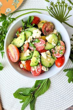 a white bowl filled with cucumber, tomatoes and feta cheese on top of a table