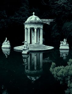 an image of a pond with statues in the water and trees around it that are reflected in the water