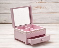 an empty pink jewelry box sitting on top of a wooden table next to a mirror