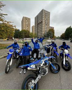 four people in blue jackets and helmets on motorbikes posing for a photo with their bikes