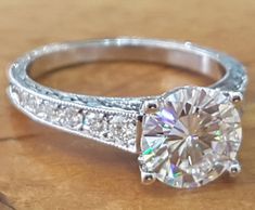 a diamond ring on a wooden table with diamonds around the band and an oval shaped center stone