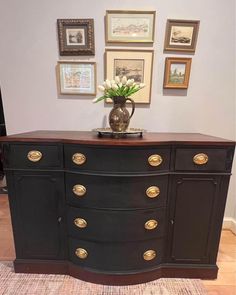 a large black dresser with gold handles and drawers in a room filled with pictures on the wall