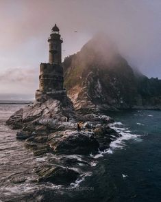 a lighthouse on top of a rocky outcropping in the ocean with fog