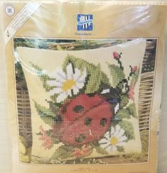 a cross stitch pillow with a ladybug and daisies on it in a package