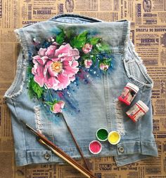 a jean jacket with flowers painted on it and paintbrushes next to the back