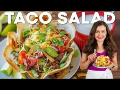 a woman holding a plate with taco salad on it next to a bowl of chips