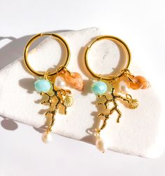 CORAL DREAMLAND Step into a world of enchantment with our "Coral Dreamland" hoop charm earrings. Imagine the gentle sway of turquoise waters captured in a light blue crystal bead, evoking the essence of tropical paradise. The 18k gold-plated coral charm adds a touch of elegance and sophistication, while the natural freshwater pearls and adorable seashell infuse a playful charm. Embrace the whimsical beauty of these earrings, reminiscent of a dreamy coral reef under the sun-kissed sea. Let your s Ocean-inspired Dangle Charms Jewelry, Ocean-inspired Gold Jewelry With Dangling Charms, Gold Ocean-inspired Jewelry With Dangling Charms, Gold Small Hoop Jewelry For The Beach, Gold Hoop Jewelry For Beach, Ocean-inspired Jewelry With Dangling Charms For Gifts, Metal Hoop Earrings With Pearl Charm For Gift, Metal Hoop Earrings With Pearl Charm As A Gift, Adjustable Small Hoop Jewelry For Vacation