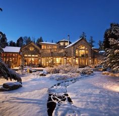 a large house surrounded by trees and snow covered ground with lights shining on the windows