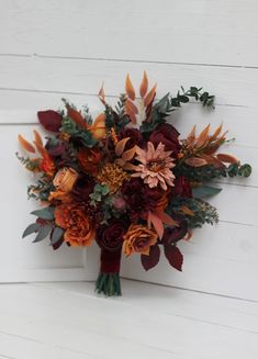 a bridal bouquet with orange and red flowers on a white wooden wall in front of a door