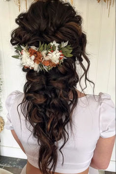 the back of a woman's head with flowers in her hair, wearing a white top