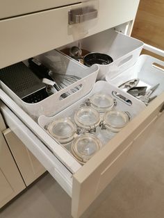 an open drawer in a kitchen with utensils and pans on the drawers