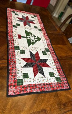 a quilted table runner on top of a wooden table with red and green decorations