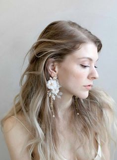 a woman with long blonde hair wearing white flowers in her hair and earrings on her head