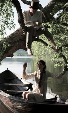 a man and woman sitting on top of a boat in the water next to a tree