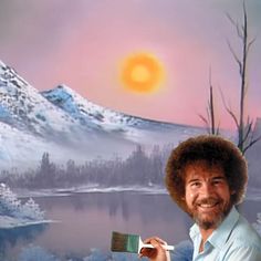 a man holding a paintbrush in front of a painting of a mountain and lake