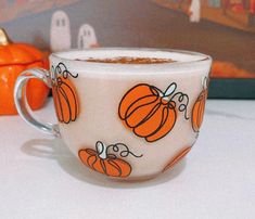 a white cup with pumpkins painted on it