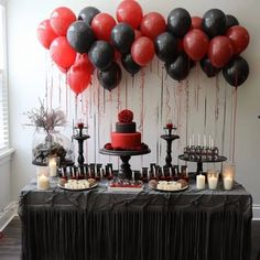 a table topped with lots of red and black balloons next to a cake on top of a plate