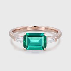 an emerald and white diamond ring with two baguettes on the side, set in rose gold