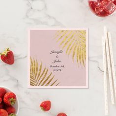 a pink and gold tropical save the date card with strawberries next to it on a marble surface